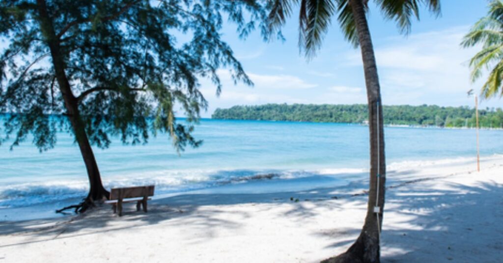 Scenic view of a tropical beach with palm trees and clear blue waters in Sihanoukville, Cambodia.